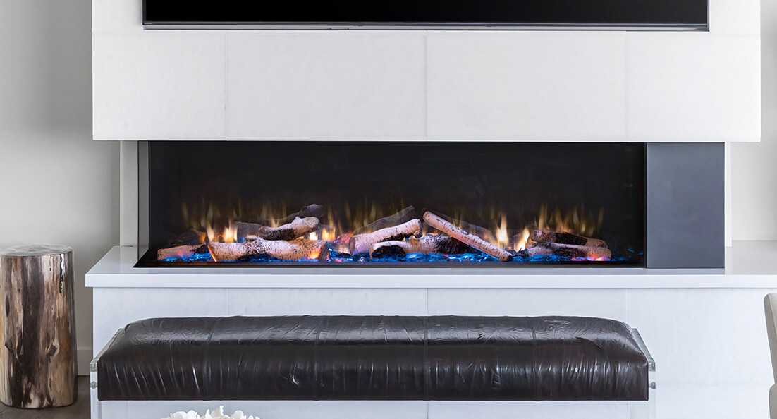 A wide multi-sided Valor electric fireplace with a long ribbon of flames and blue accent glow, set into a white surround in a minimalist open-plan living space