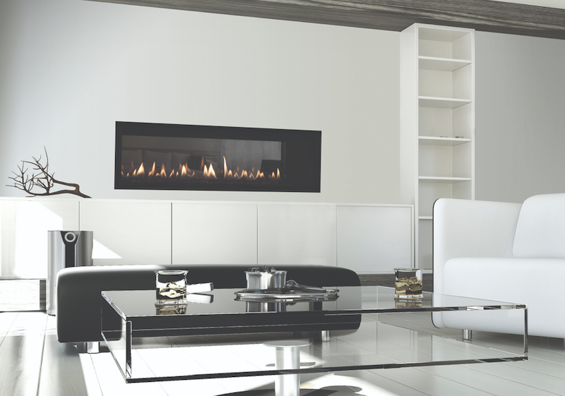 A modern living room with a sleek black rectangular fireplace set in a white wall. Glass walls provide an airy feel, while a glass coffee table with a metallic base sits in front of the white and black sofa. The table holds two glasses, a small plate with snacks, and a decorative branch. Shelving unit in the back.