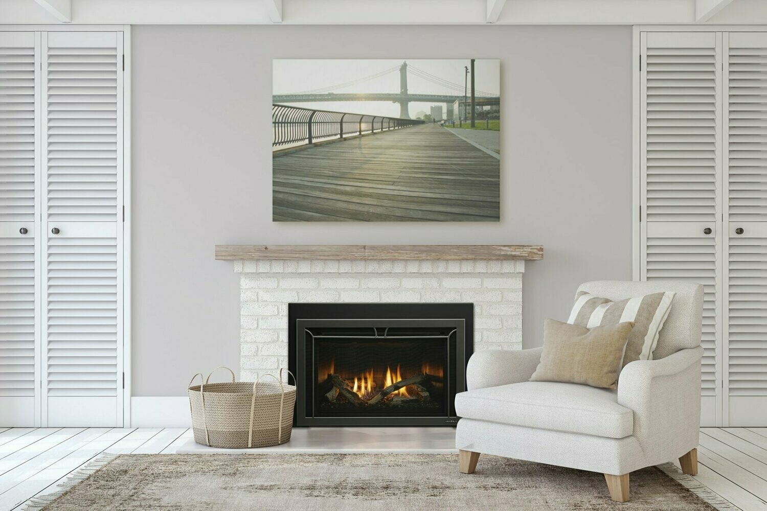 A cozy living room with a white brick fireplace and a crackling fire. Above the mantel hangs a framed photograph of a boardwalk with a bridge in the background. Glass walls provide an airy feel, while to the right, a cushioned armchair with a throw pillow invites relaxation. A woven basket sits to the left of the fireplace.