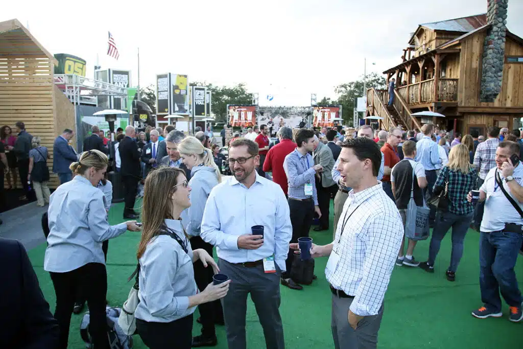 People networking at an outdoor event with booths in the background.