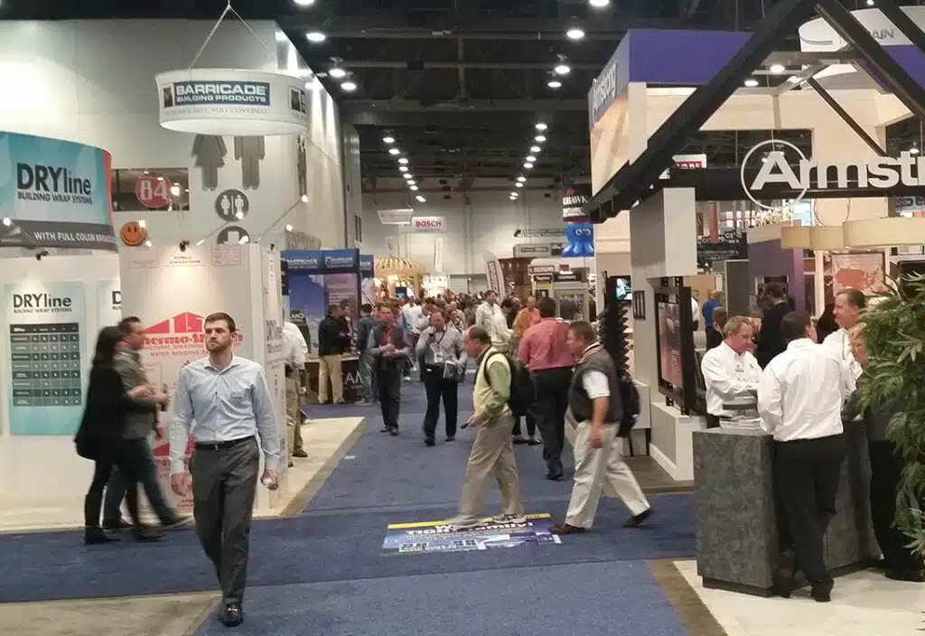 People walking through a busy trade show with booths and banners displayed.