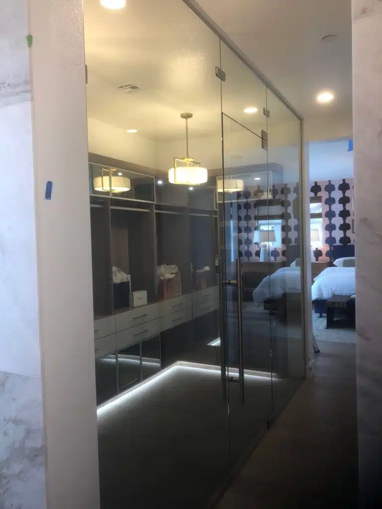 Glass closet doors leading to a walk-in closet with shelves and drawers.