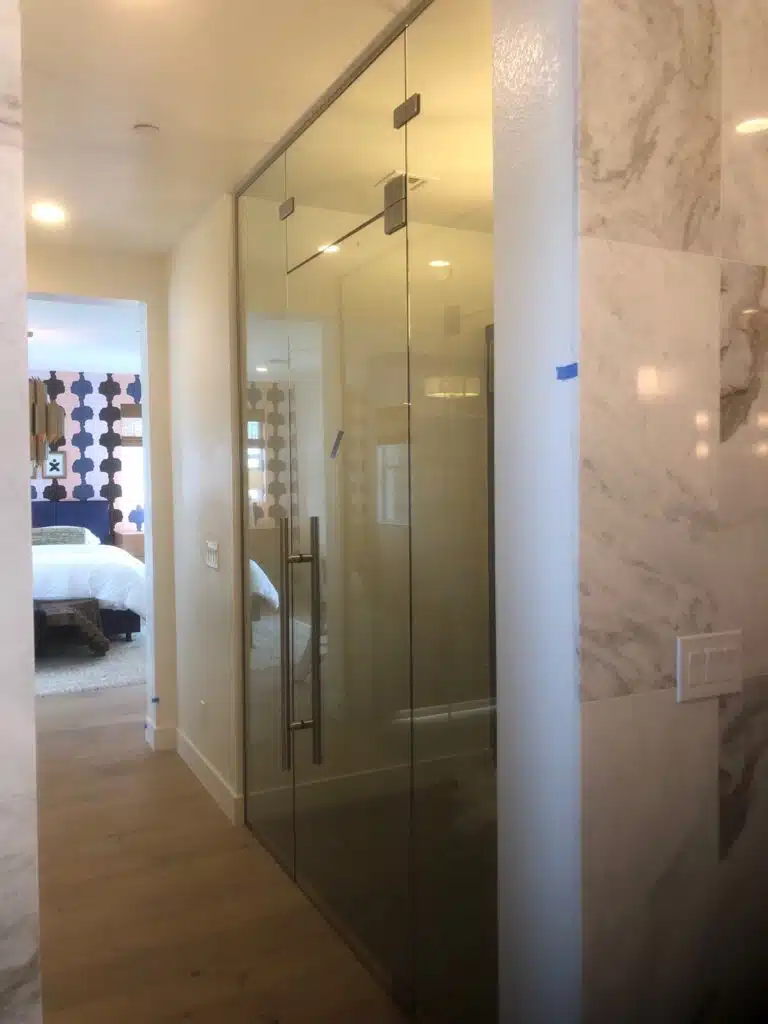 Glass door with metal handles, leading to a bedroom, with marble walls on either side.