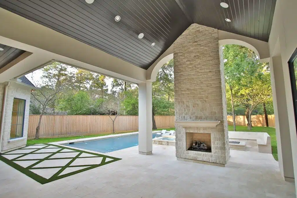 Luxury outdoor patio with a tall stone fireplace, covered ceiling, and a poolside view.