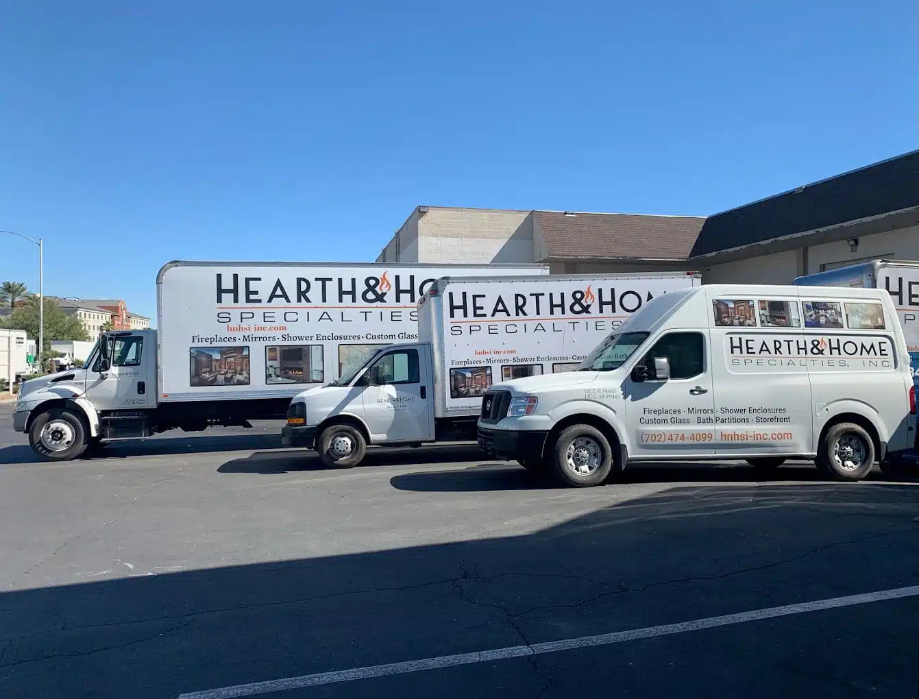 Three service vehicles marked with signs for "Hearth & Home Specialties." are parked in a lot. The vehicles include a large truck, a medium-sized van, and a smaller van. Each vehicle displays images and text promoting fireplaces, mirrors, shower enclosures, and custom glass—truly embodying our About Us vision.