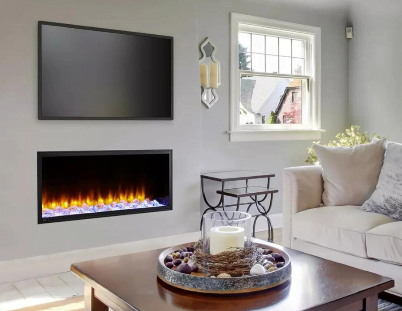 A cozy living room showcasing exquisite interior design features a wall-mounted flat-screen TV above a sleek electric fireplace. A large window lets in natural light, illuminating a plush sofa with a pillow. In the foreground, a coffee table is adorned with a decorative centerpiece, enhancing the home's warm ambiance.