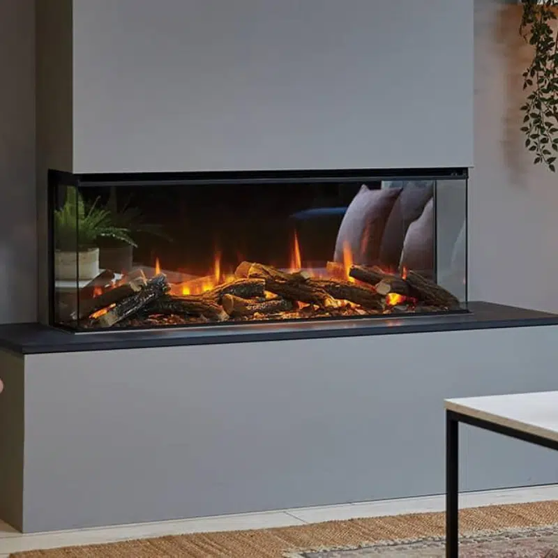 Modern wall-mounted electric fireplace with lifelike glowing logs and flames, set against a sleek gray wall. To the left, a small potted plant adds greenery. A light-colored rug and part of a white table are visible in the foreground.