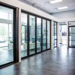 A modern office space in Las Vegas features a polished concrete floor and custom glass partitions. Several rooms are divided by floor-to-ceiling glass doors, allowing natural light to flood in. A seating area is visible through the glass, creating an inviting atmosphere.