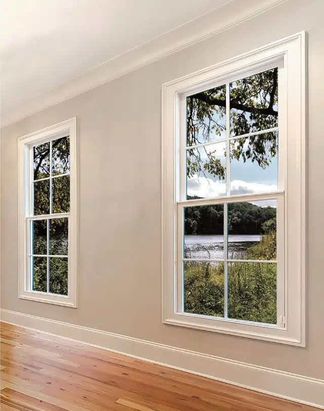 A room with two large windows, showcasing a scenic view of a river, trees, and a cloudy sky. The space features light-colored walls and wooden flooring, complemented by a custom glass design that enhances its elegance.