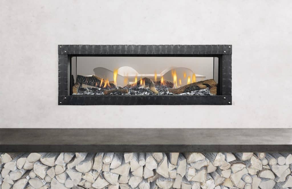 A modern rectangular fireplace with a black frame is set into a white wall. It showcases vibrant flames and glowing logs. Below, there is a storage area filled with stacked, cut firewood.